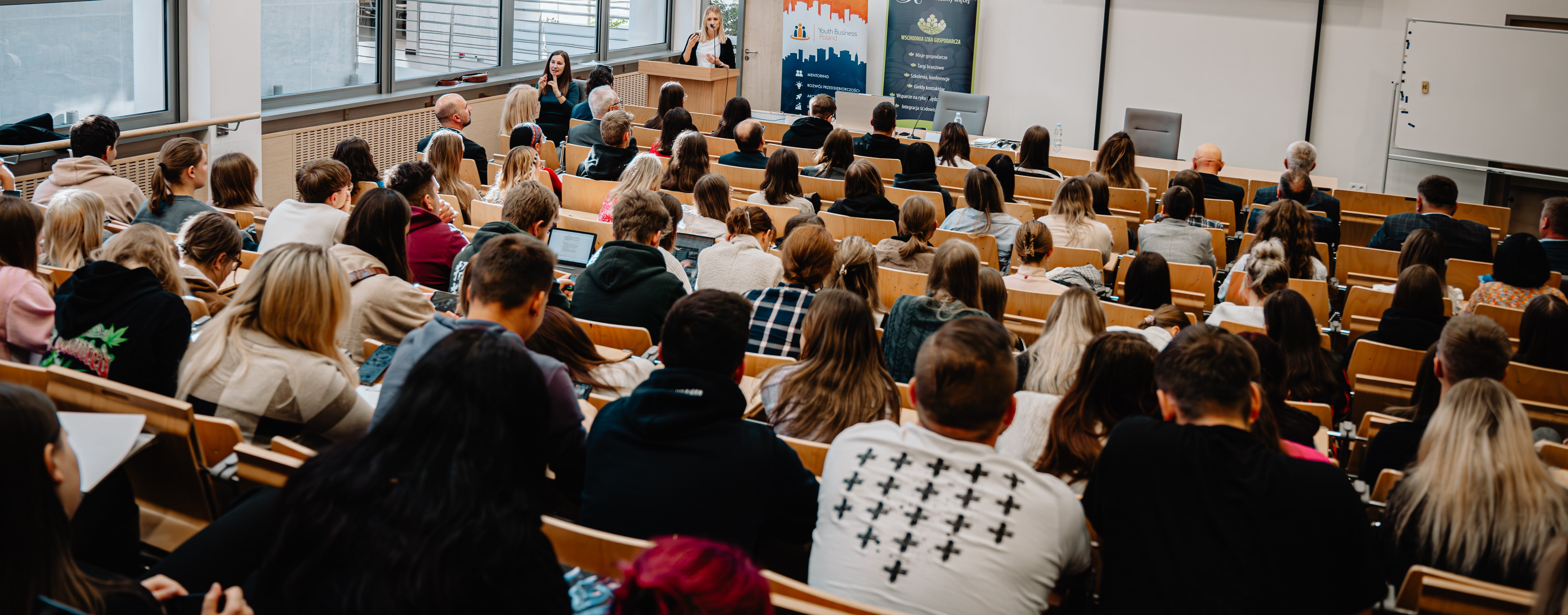Osoby siedzą w auli i słuchają wykładu.