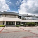 Biblioteka Główna Uniwersytetu w Siedlcach - Nowoczesny budynek Biblioteki Głównej Uniwersytetu w Siedlcach z przeszkloną fasadą i szerokim placem z czerwono-szarymi wzorami z kostki brukowej..