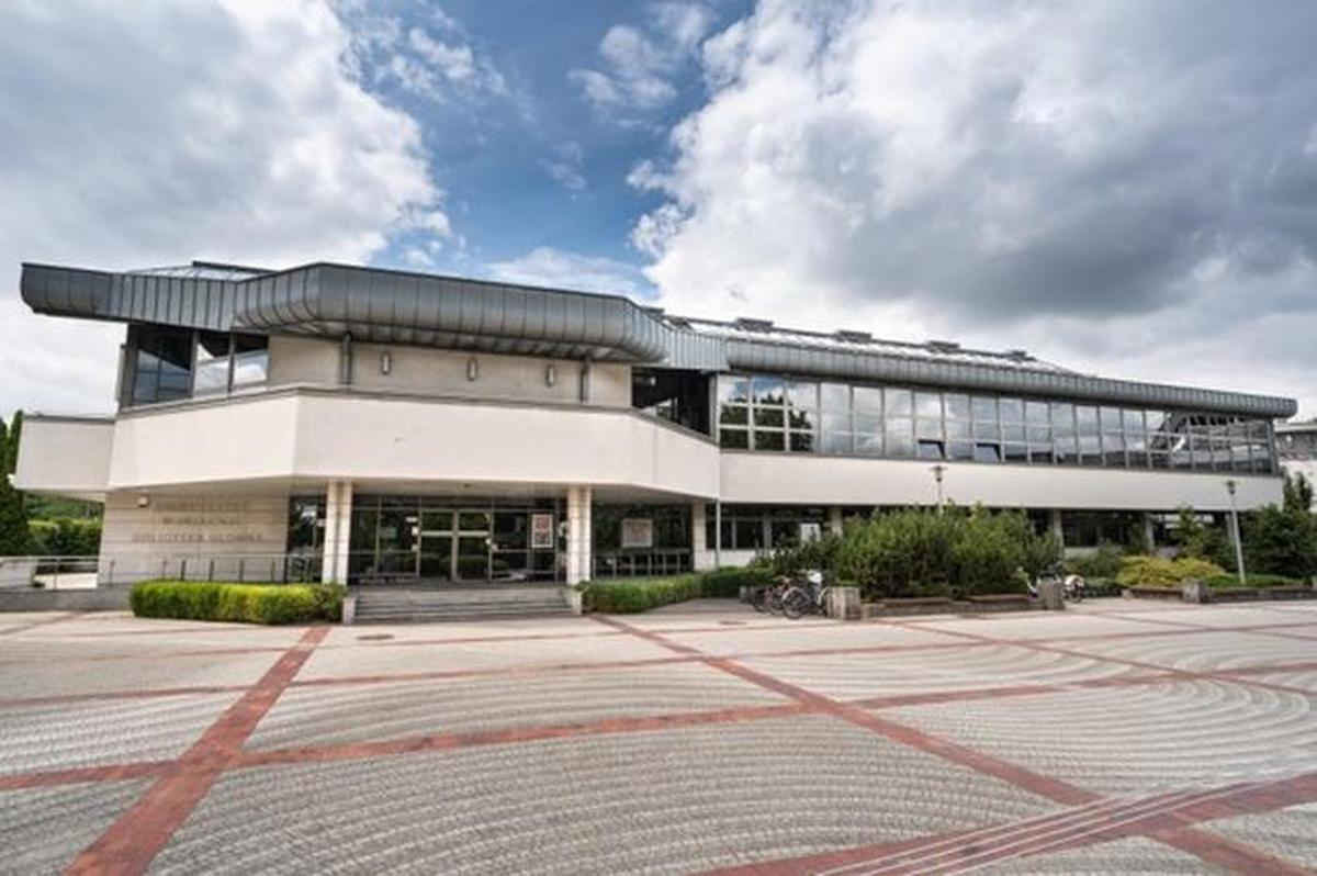 Biblioteka Główna Uniwersytetu w Siedlcach - Nowoczesny budynek Biblioteki Głównej Uniwersytetu w Siedlcach z przeszkloną fasadą i szerokim placem z czerwono-szarymi wzorami z kostki brukowej..